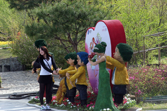커풀룩을 차려 입은 젊은 남녀가 마스코트 모형 앞에서 포즈를 취하고 있다.